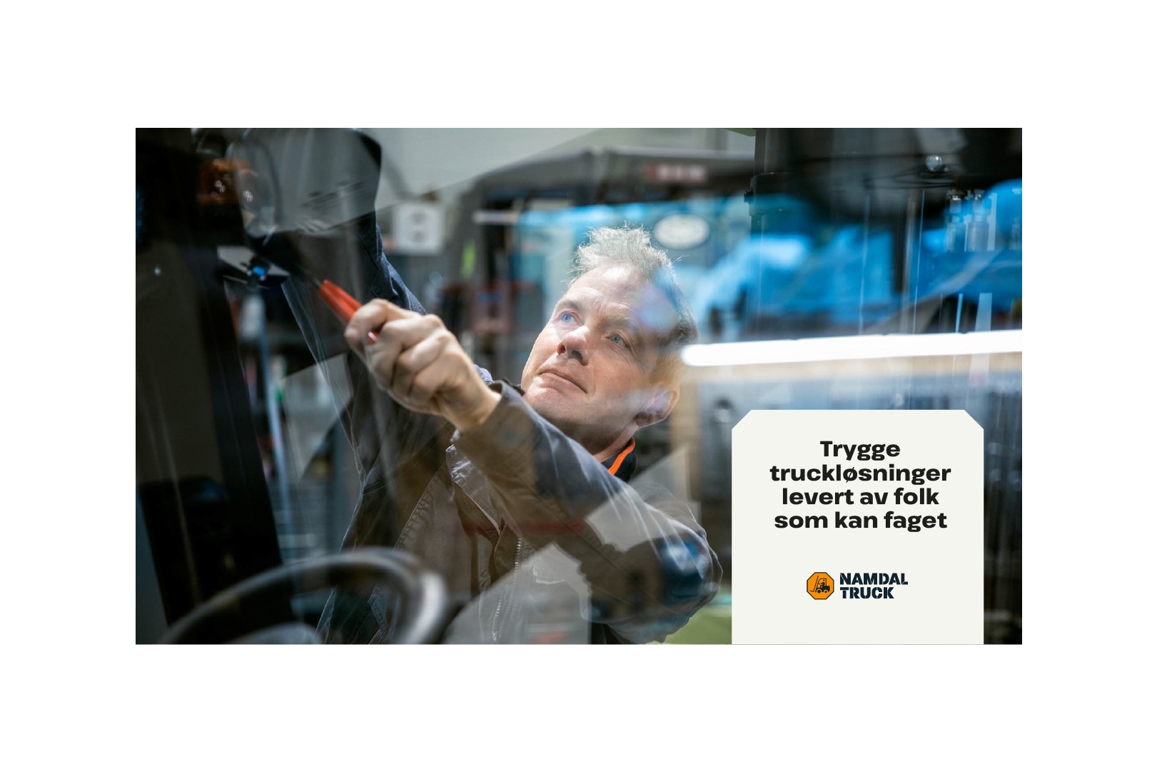 En mann med verktøy skrur på en truck med en tekstplakat liggende over bildet