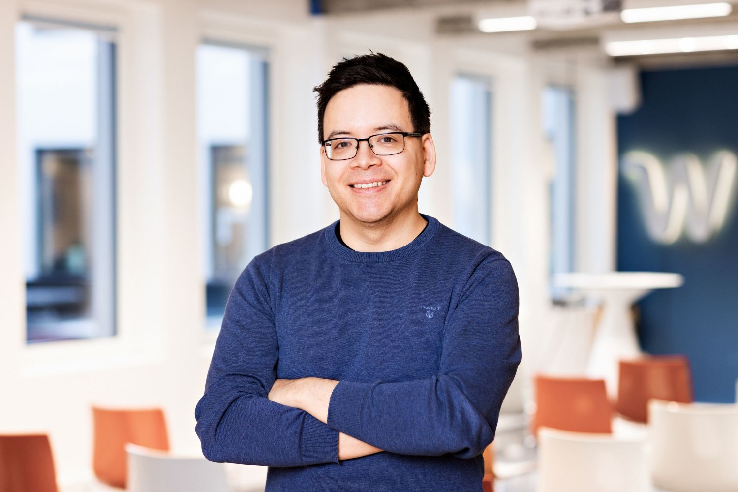 Portrettbilde av en mann med briller som smiler i et moderne kontorlandskap