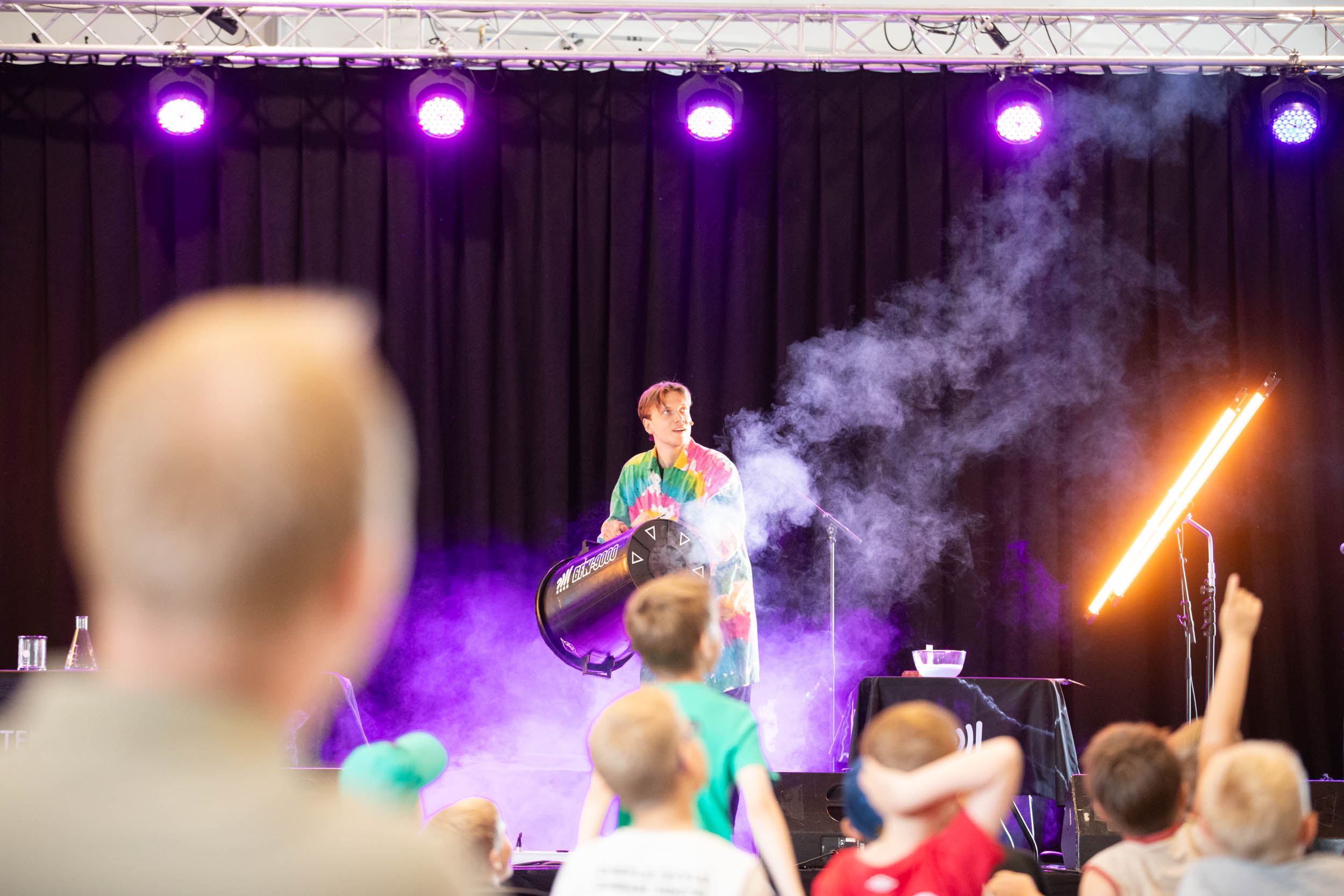 En fargerik person står på en scene og lager show mens publikum ser på
