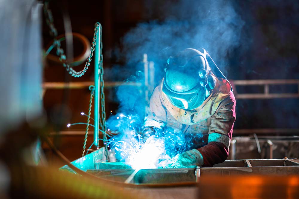 En person i heldrakt som står og sveiser, mye røyk siver opp 
