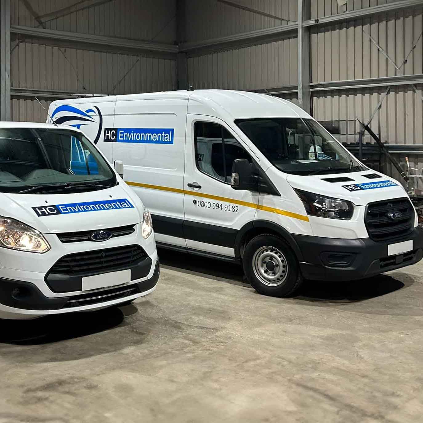 Two white vans with HC Environmental branding parked inside a warehouse.