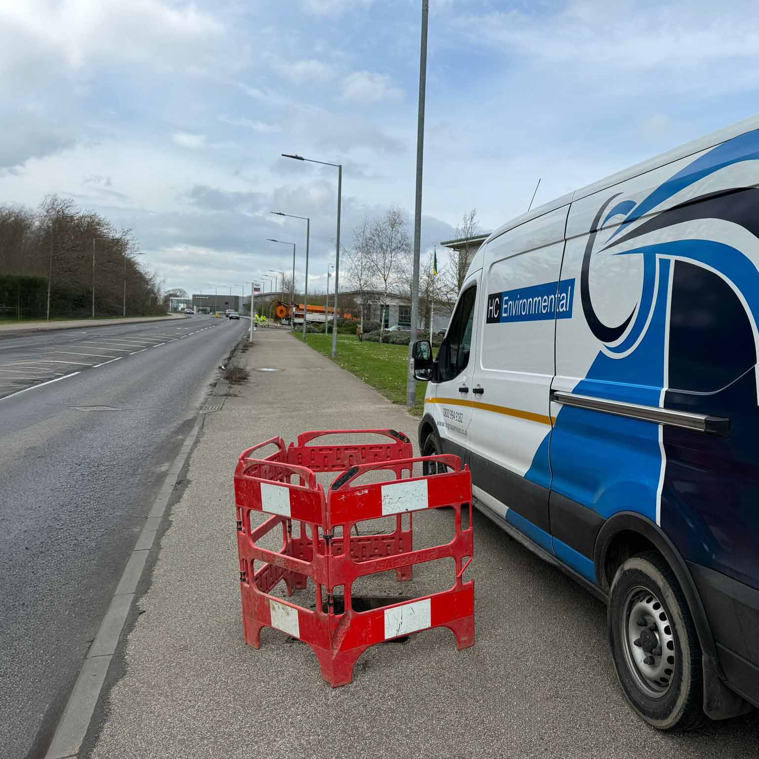 HC Environmental van parked on a roadside next to red safety barriers with a cloudy sky overhead.