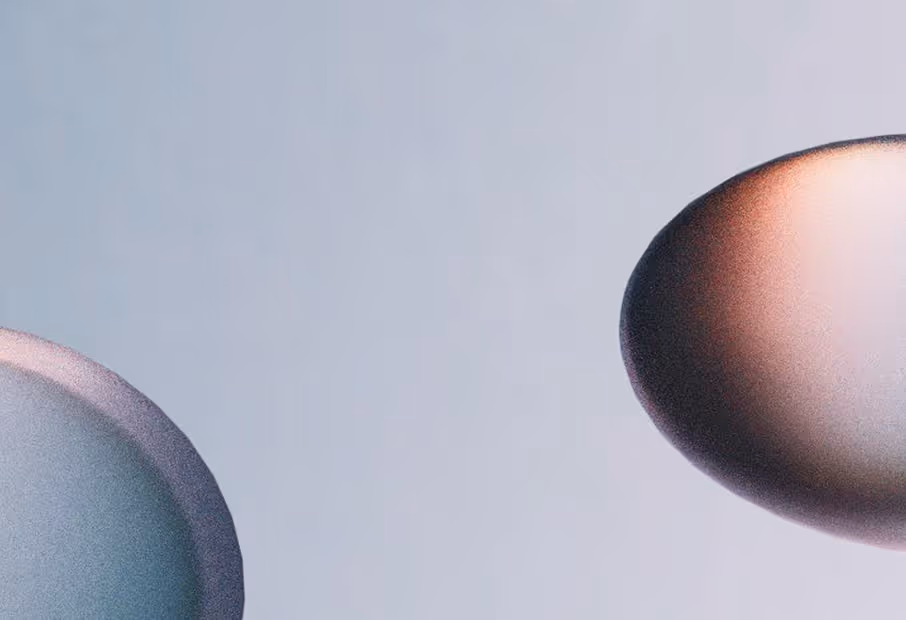 Close-up of two spherical objects, one on the left with a blue-gray hue and one on the right with a copper-like gradient, set against a pale blue background.