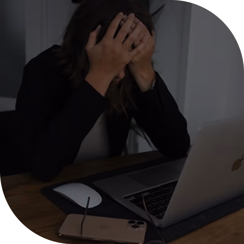 Person sitting at a desk with a laptop and smartphone, holding their head in their hands in frustration.