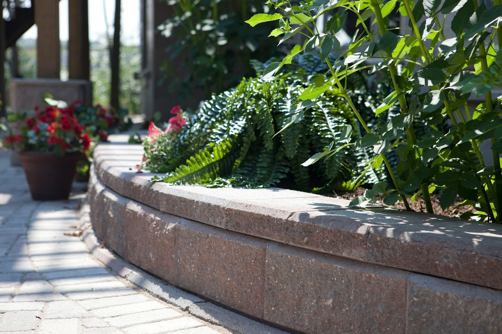 Curved Allan Block retaining wall with coping and a split-face texture forming a raised planter beside a paved walkway