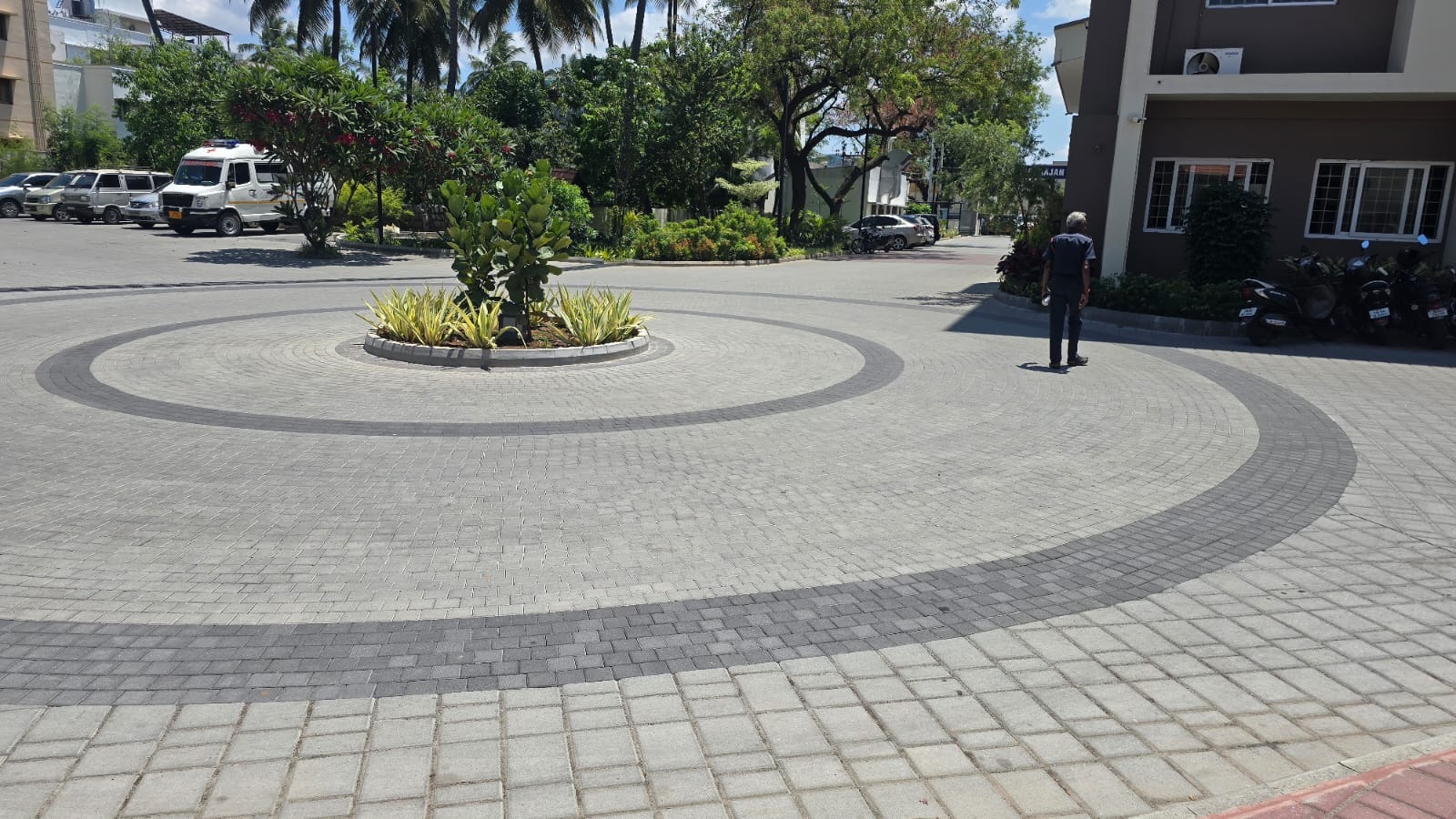 Residential driveway of grey concrete pavers with a circular pattern of darker bands around a central planted island