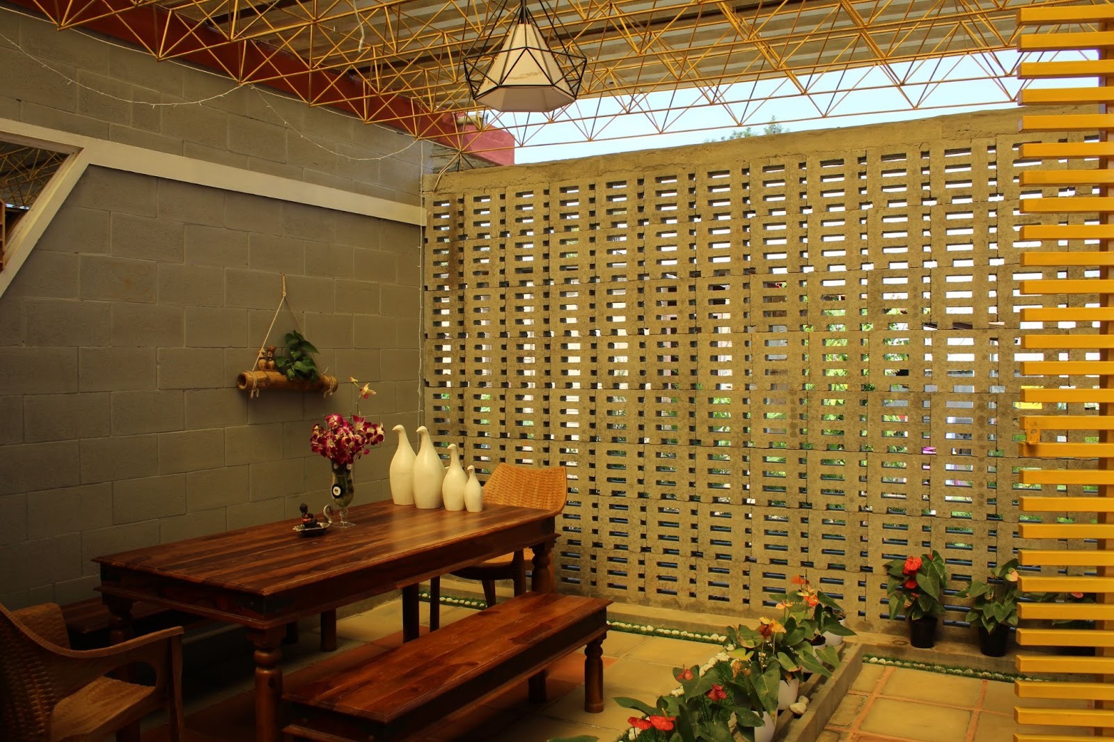 Covered dining area with a wooden table and benches before a screen wall of stacked concrete blocks with open gaps