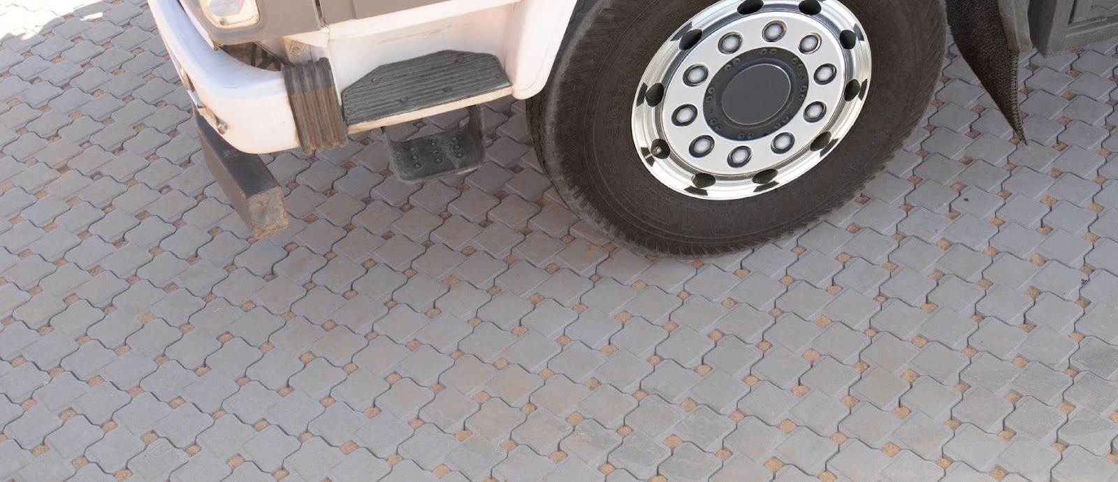 Truck wheel resting on grey interlocking concrete pavers in a close-up of a paved vehicle area