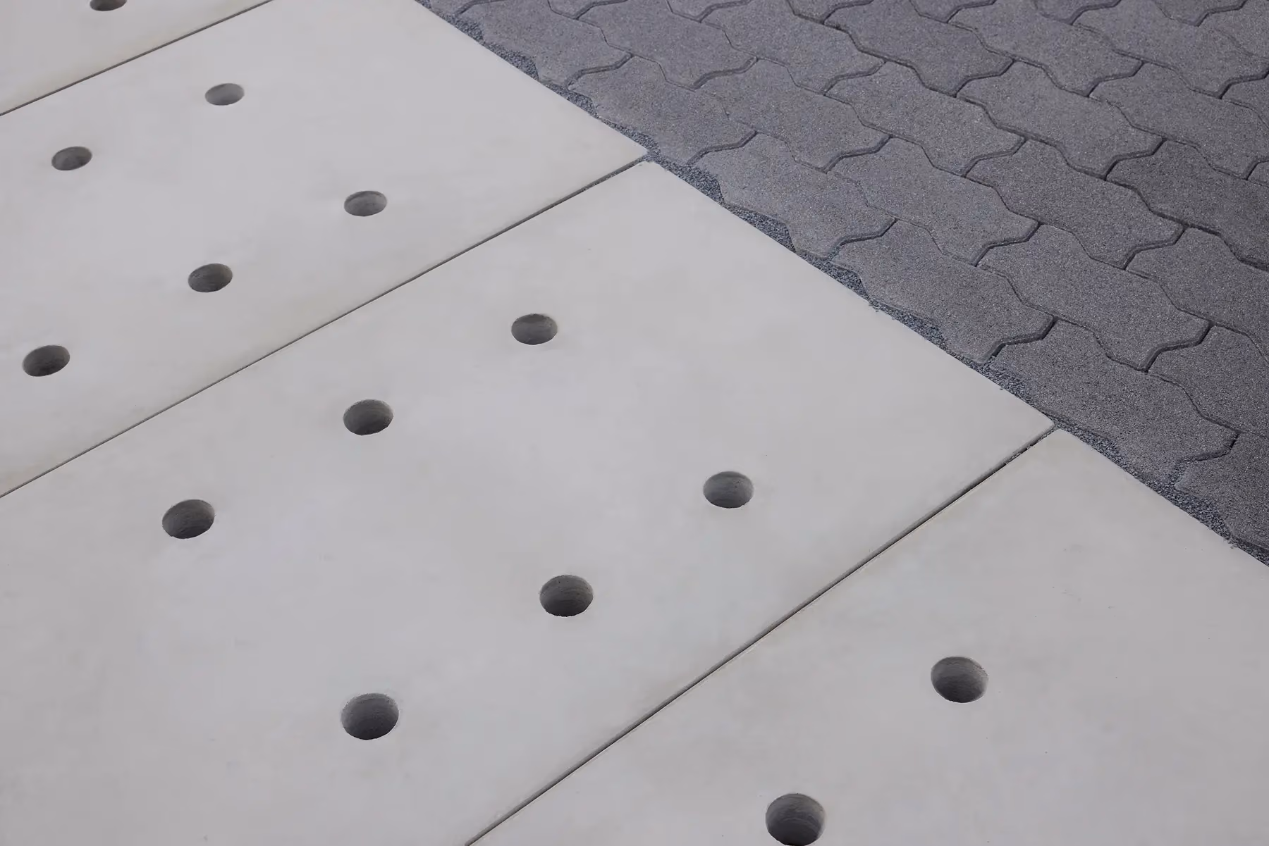Precast Drainage Slabs with two rows of round holes laid beside grey interlocking pavers on a paved pathway