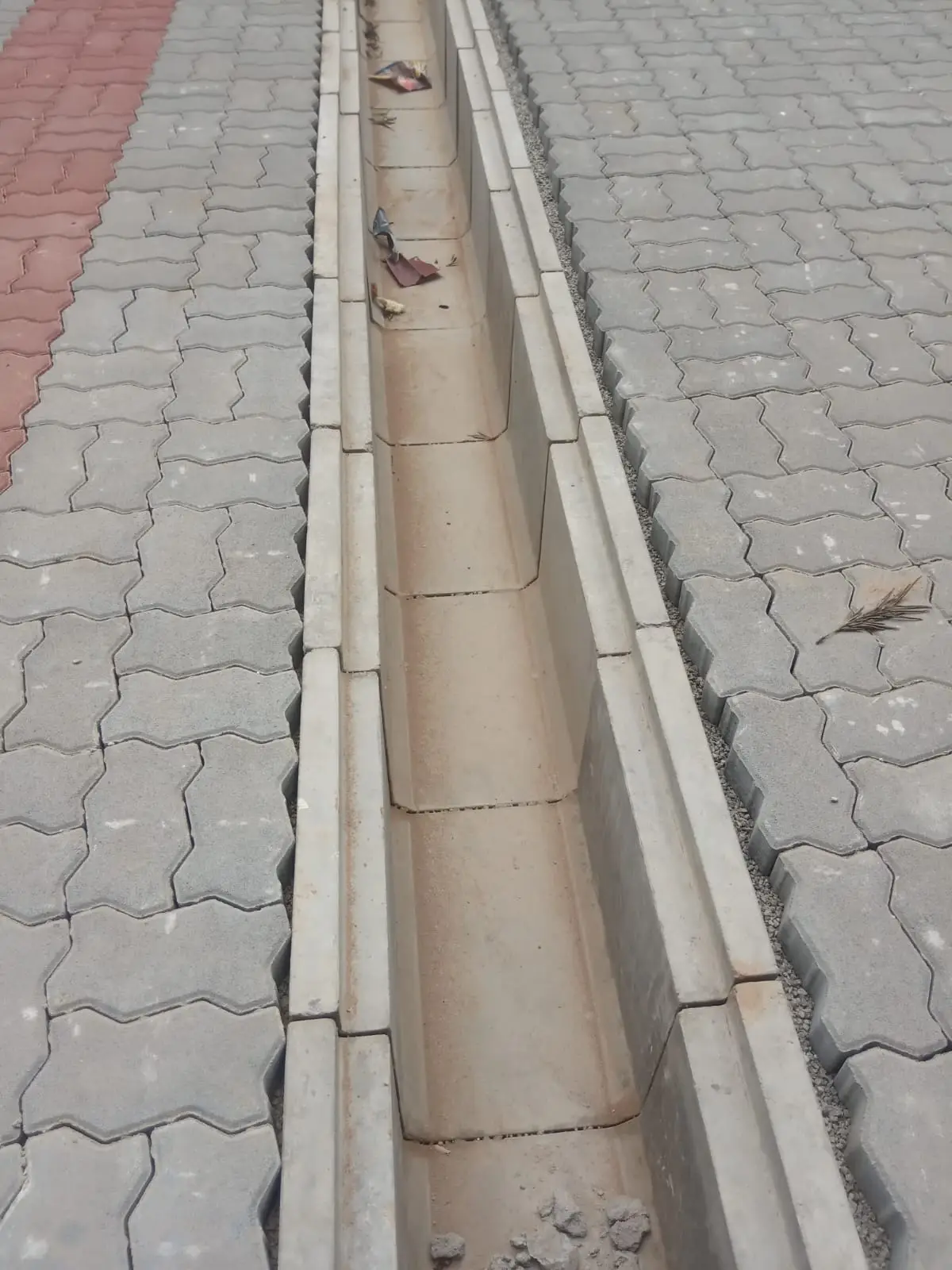 Precast U-shape drain installed in a run between grey interlocking concrete pavers