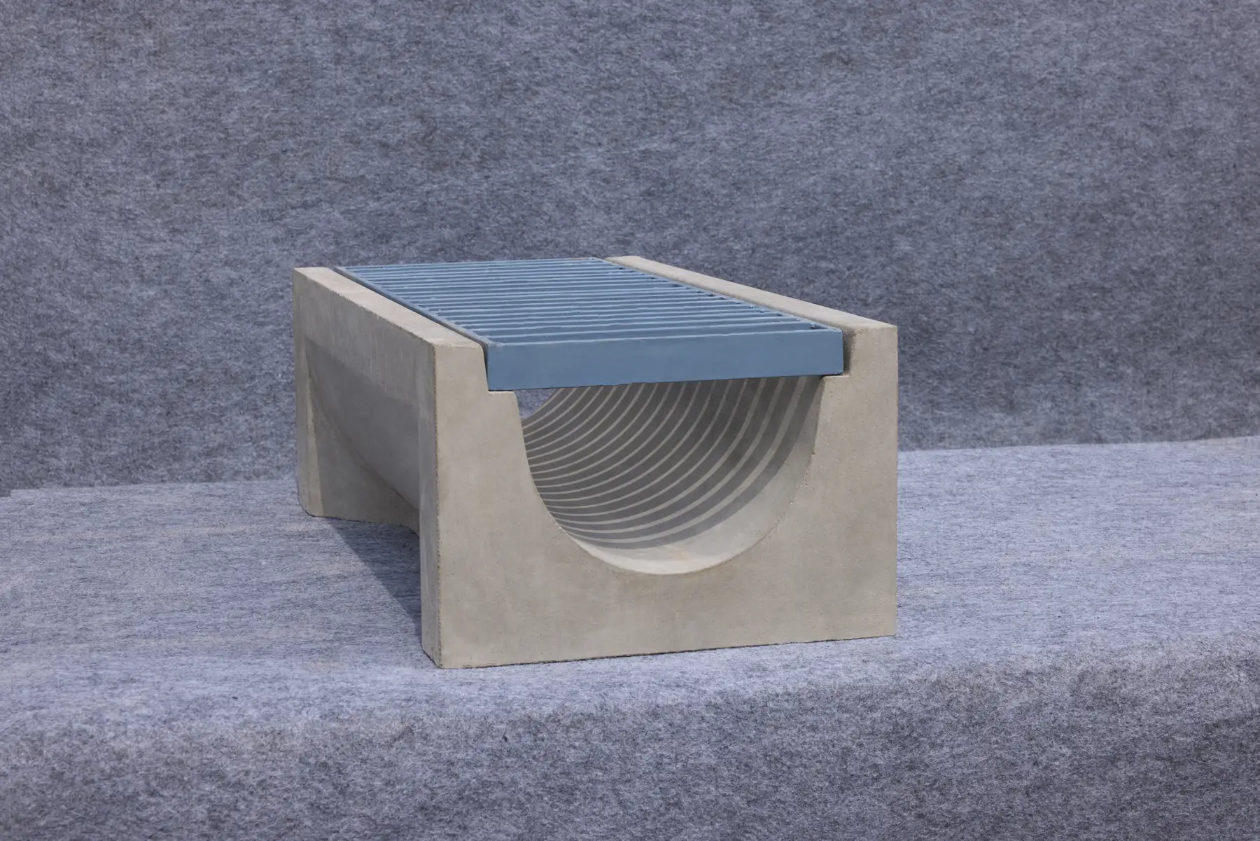 Precast U-shape drain in grey concrete topped with a blue metal grating, side view