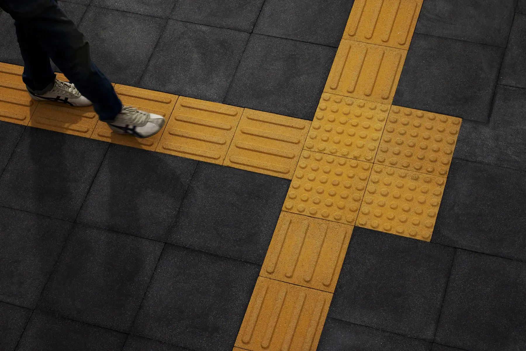Yellow tactile direction and warning concrete paving tiles with raised bars and dots set into dark grey paving