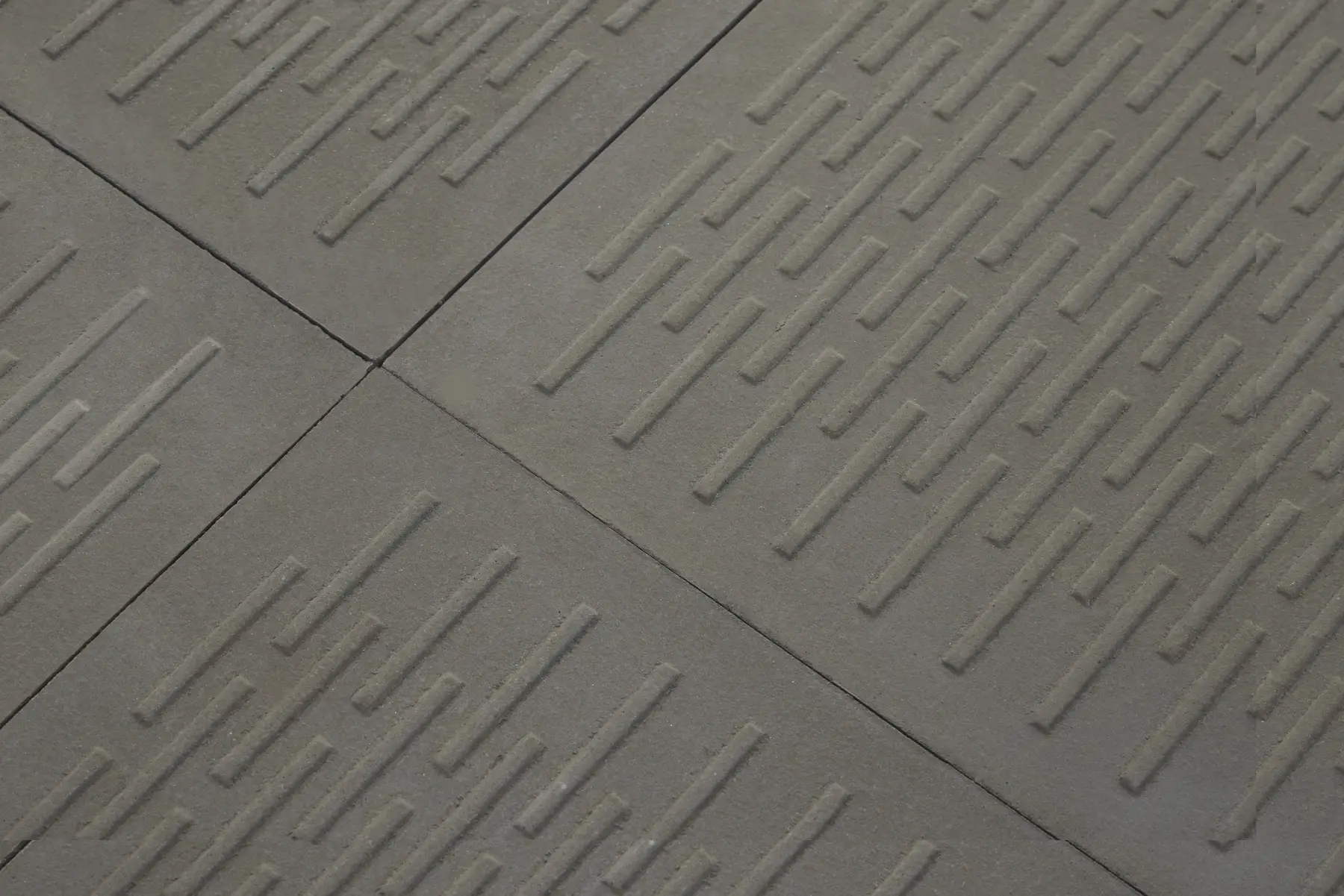 Close-up of grey concrete paving tiles with a raised linear groove pattern