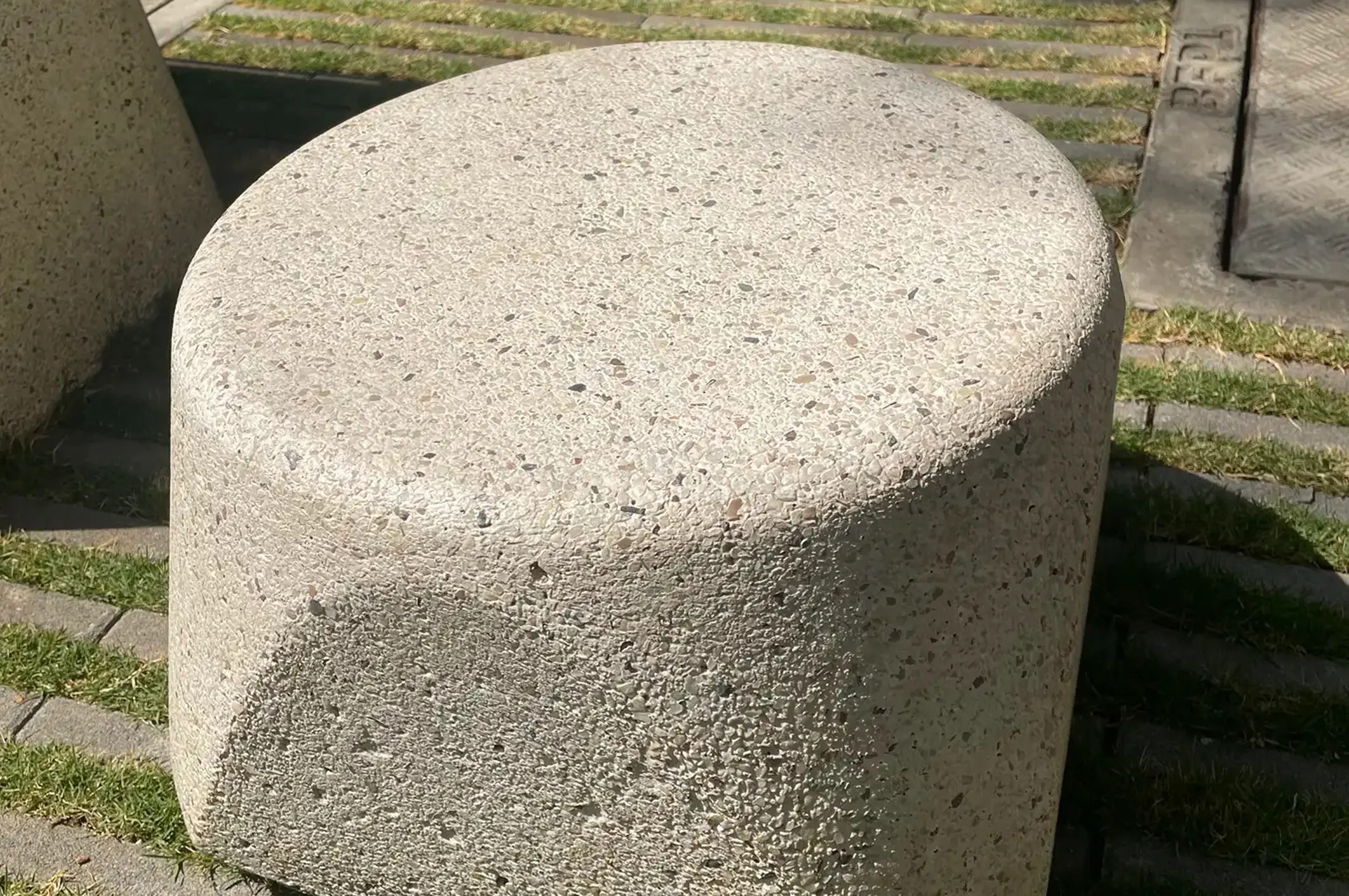 Rounded precast concrete bollard with an exposed-aggregate finish beside a grass-paver surface