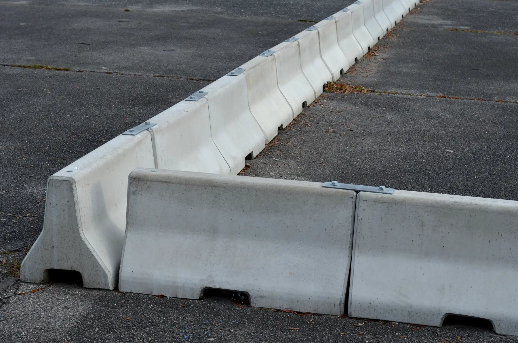 Modular precast concrete jersey barriers lined up on an asphalt road, showing interlocking joints and tapered profiles