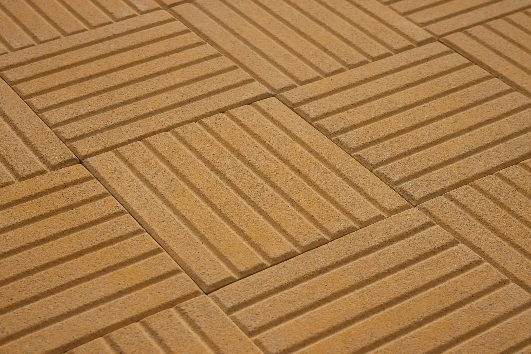 Close-up of yellow 6-line concrete paving tiles with six evenly spaced grooves, laid in an alternating grid pattern