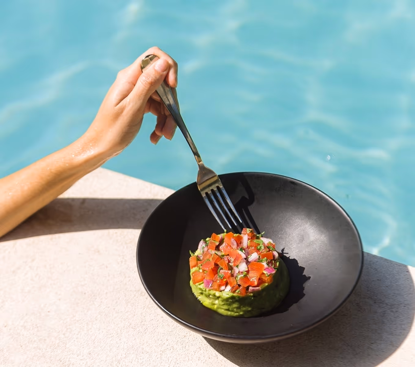 Tartar de aguacate fresco servido en un bol negro junto a la piscina turquesa del hotel La Valise Los Cabos.
