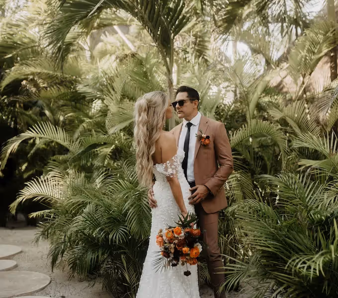 Una pareja de novios abrazándose en los exuberantes jardines tropicales del hotel La Valise Los Cabos en México.