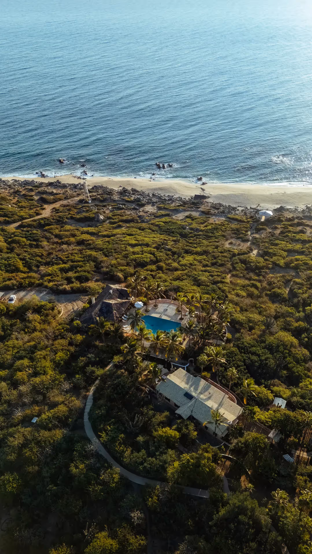 Vista aérea de la playa de arena blanca y la arquitectura tropical del hotel La Valise Los Cabos ubicado en la jungla.