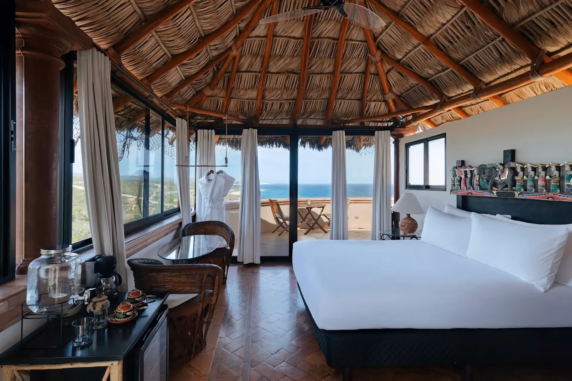 Luxury bedroom under a traditional palapa roof with panoramic ocean views at La Valise Los Cabos hotel.