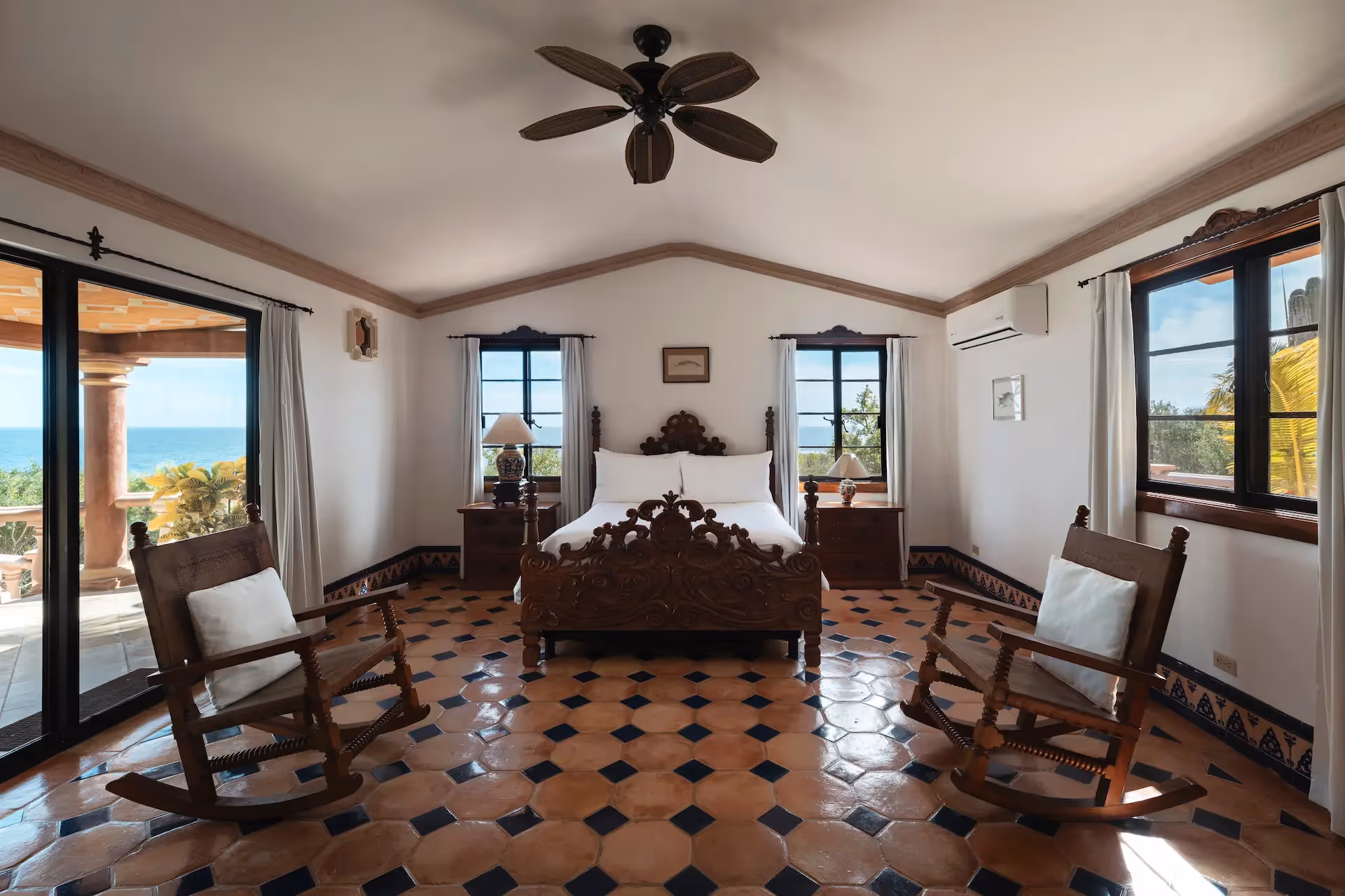 Spacious suite with a carved wooden bed, rocking chairs, and a private terrace overlooking the sea at La Valise Los Cabos hotel.