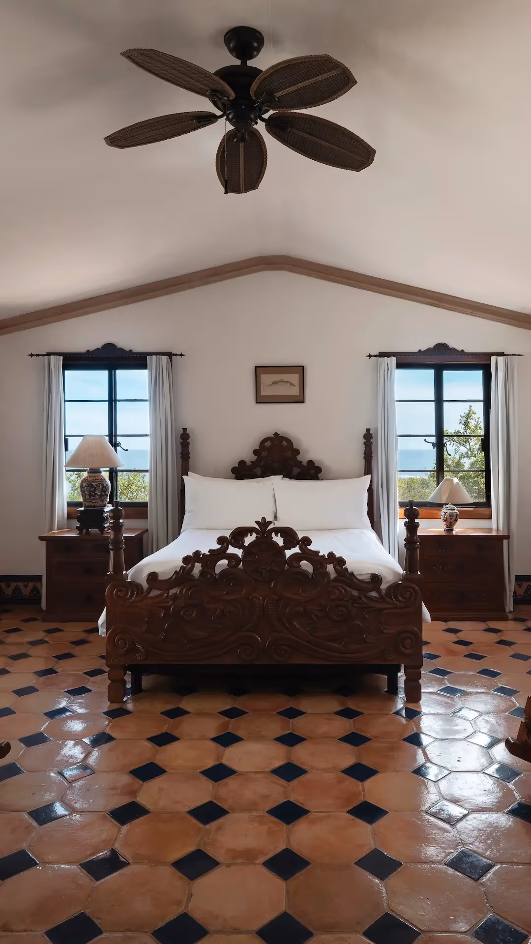 Spacious suite with a carved wooden bed, rocking chairs, and a private terrace overlooking the sea at La Valise Los Cabos hotel.