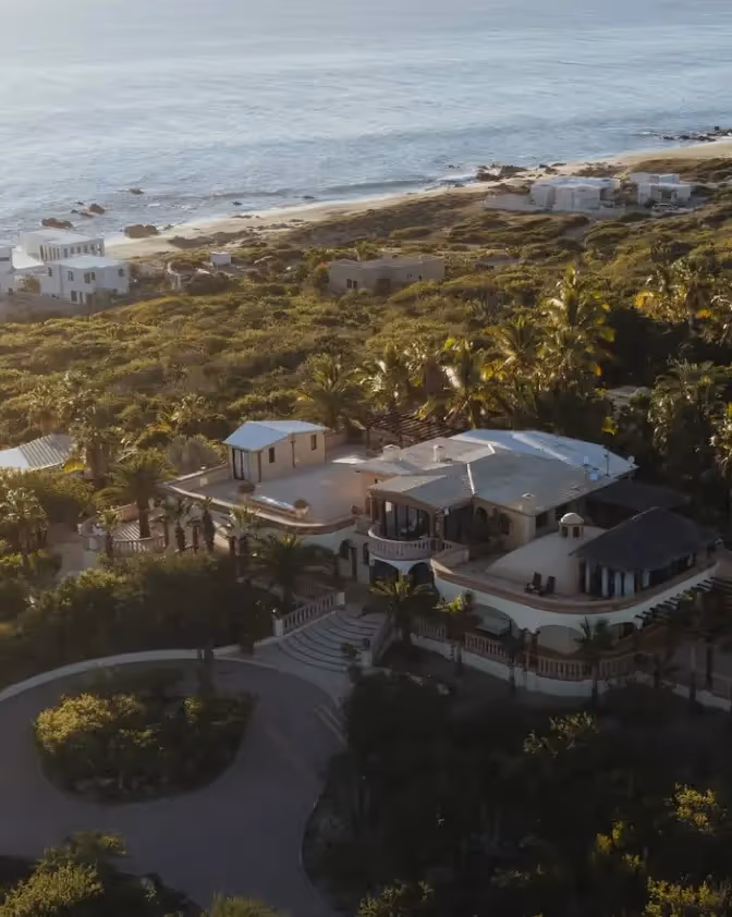 Suite de lujo en el hotel La Valise Los Cabos en México, con un diseño interior boho-chic con vigas de madera en el techo, sillas hechas a mano e iluminación ambiental cálida.
