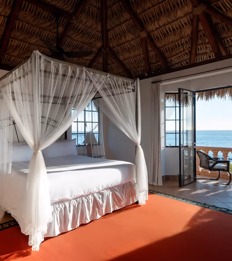 Suite de lujo con cama con dosel y techo de palapa tradicional con techo de paja en el hotel La Valise Los Cabos.