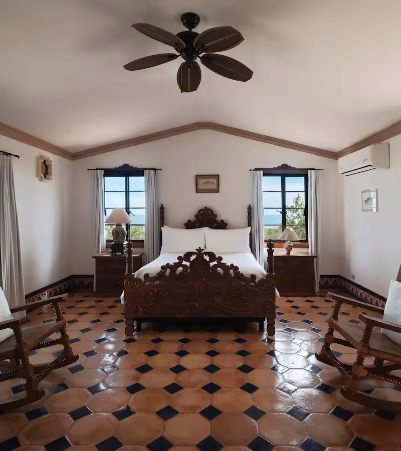 Amplia suite con una cama de madera tallada, mecedoras y una terraza privada con vista al mar en el hotel La Valise Los Cabos.