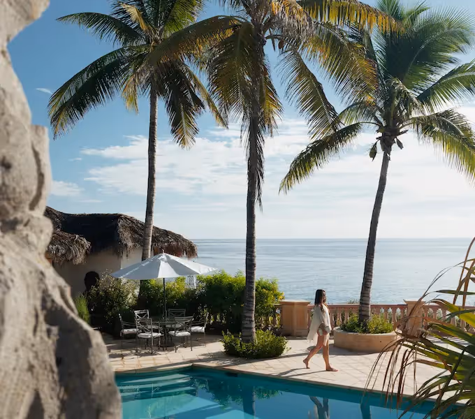 Vista desde arriba de una mujer con sombrero para el sol caminando junto a una piscina turquesa en el hotel La Valise Los Cabos.