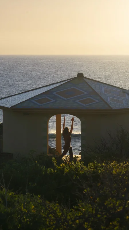 Mujer practicando yoga frente al océano durante una puesta de sol dorada en el hotel La Valise Los Cabos.