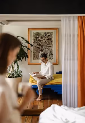A couple relaxing in a luxury suite at La Valise Mexico City hotel, with a man reading on the bed and a woman in the foreground.