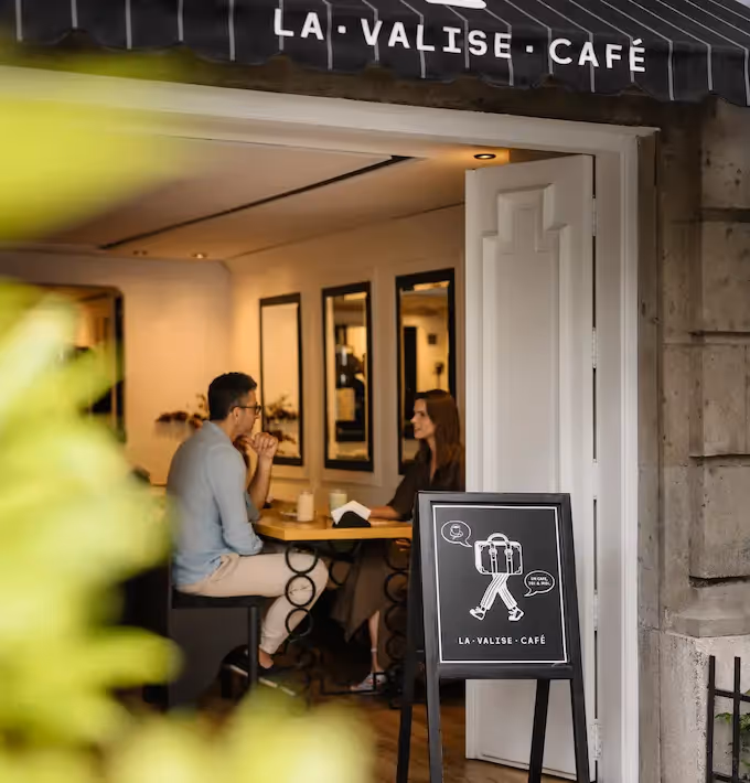 Couple enjoying coffee at La Valise Mexico City hotel restaurant terrace, showing the stylish entrance with signage and a chalkboard menu.