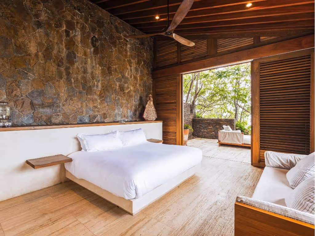 Spacious hotel room featuring a natural rock wall, crisp white bedding, and a private terrace at La Valise Mazunte Hotel.