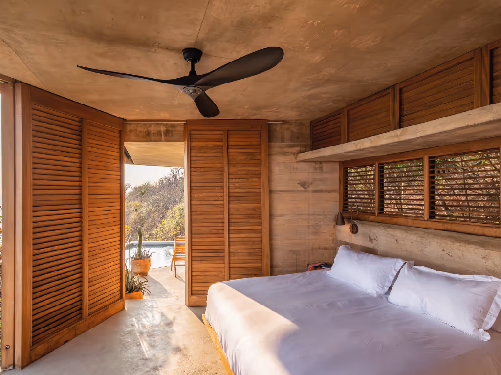 Luxury bedroom at La Valise Mazunte Hotel featuring rammed earth walls, a black ceiling fan, and a view of the outdoor pool.