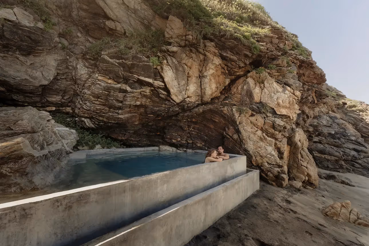 A couple enjoying a romantic moment in the infinity pool at La Valise Mazunte Hotel, overlooking the Pacific Ocean by a rocky cliffside.