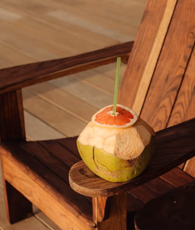 Fresh chilled coconut drink with a straw on a wooden lounge chair at La Valise Mazunte Hotel.