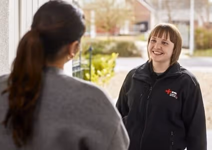 A woman in a Red Cross uniform smiling and talking to another woman at a doorway.