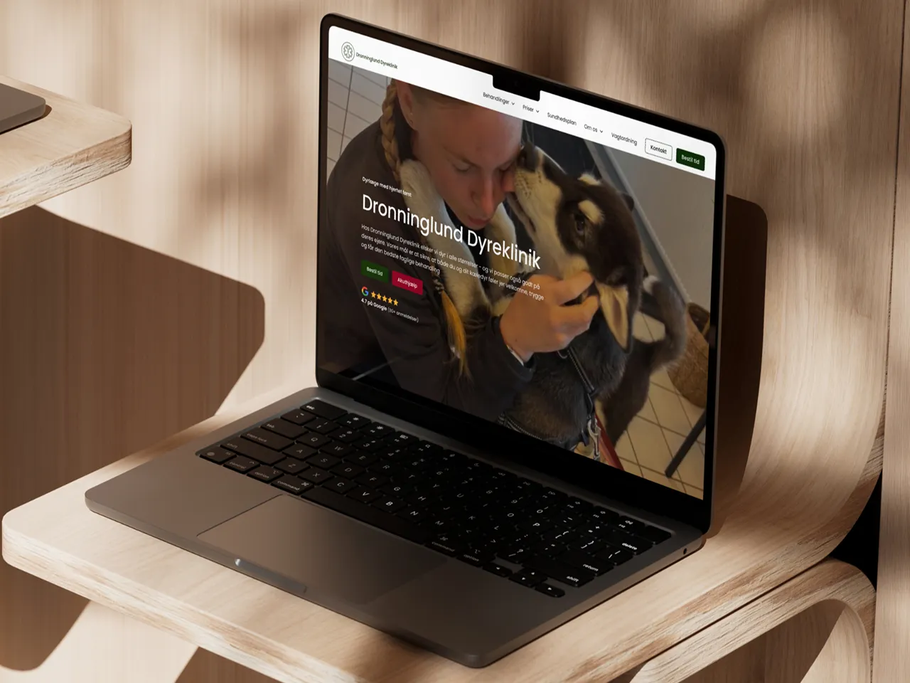 Bærbar computer på et lyst træbord med vist på skærmen til Dronninglund Dyreklinik nye hjemmeside.