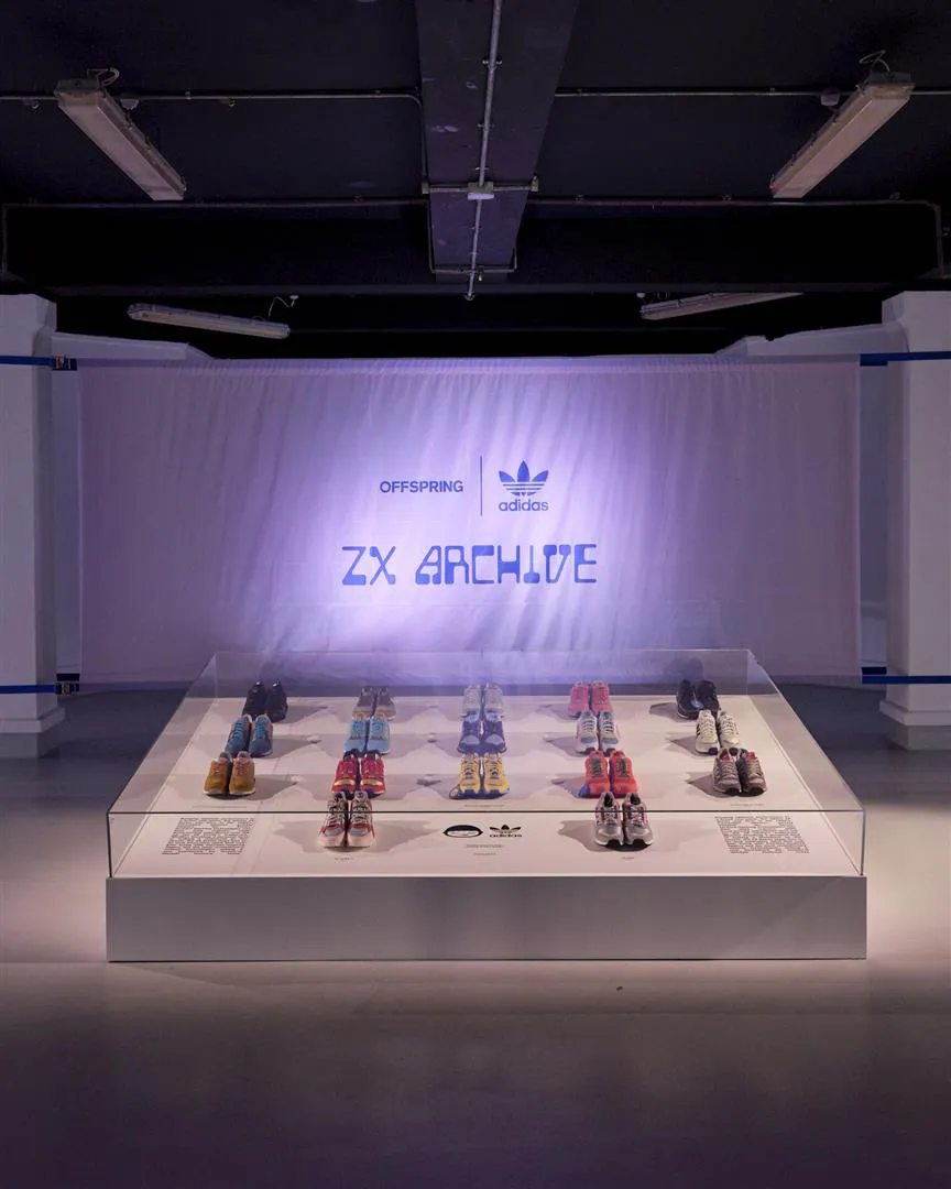 Exhibition display of various Adidas ZX Archive sneakers arranged in rows inside a glass case with a lit backdrop featuring Offspring and Adidas logos.