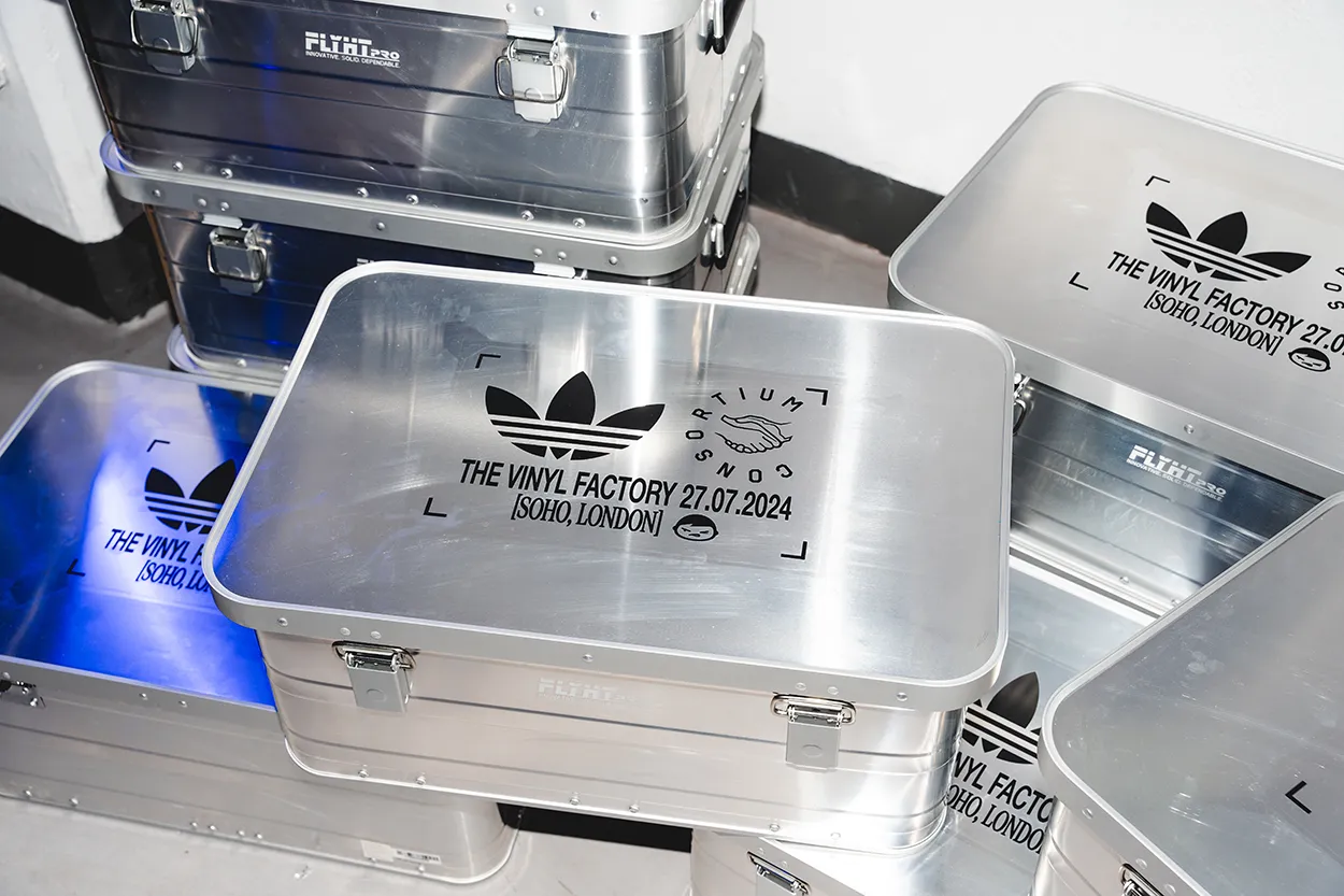 Metal storage cases with black Adidas logo and text reading 'The Vinyl Factory 27.07.2024 [Soho, London]' stacked indoors.