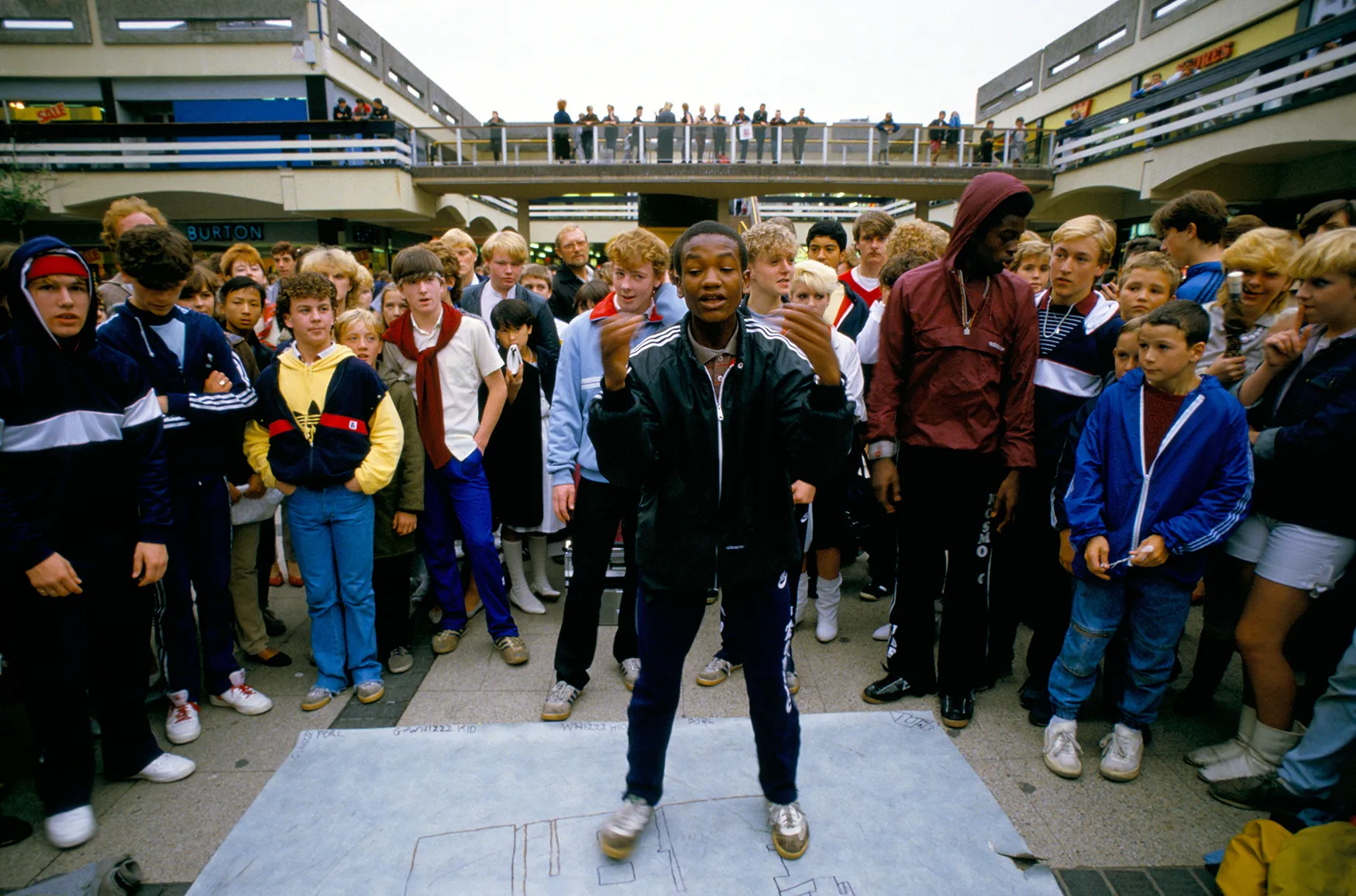 Archive image from the late 1980s showing a teenager breakdancing in adidas trainers in a city centre.