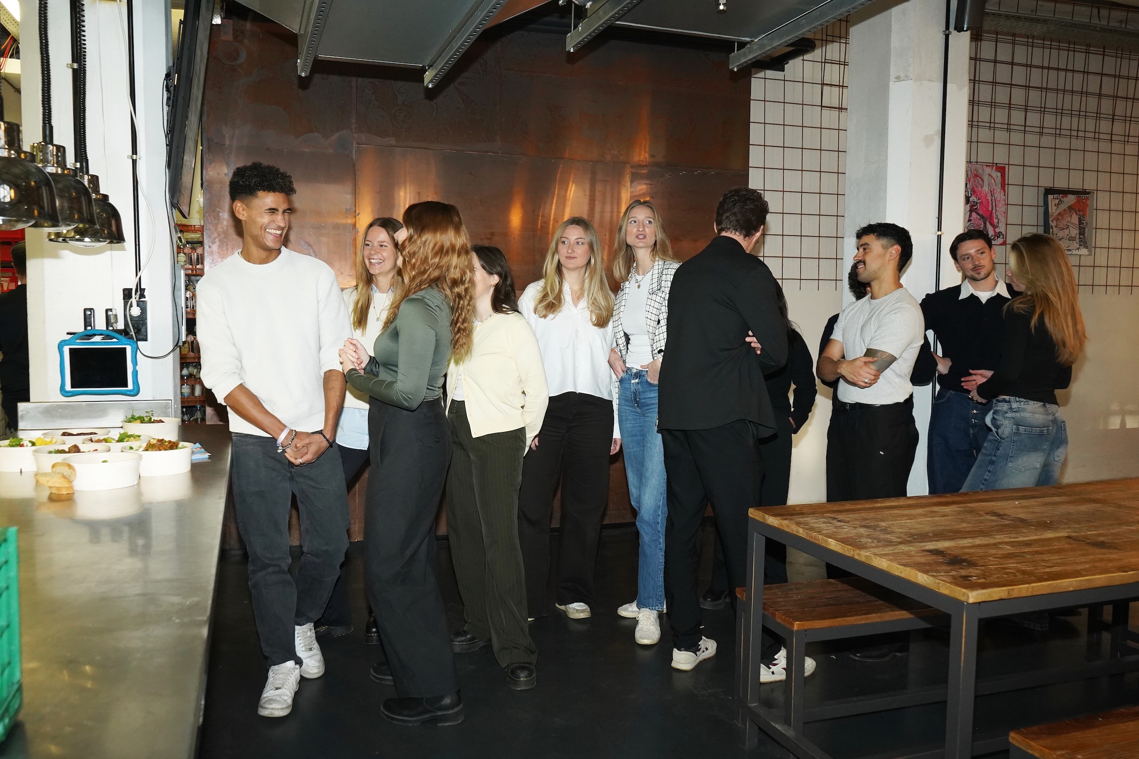 Eine Gruppe junger Menschen unterhält sich in einem modernen Innenraum neben einem Holztisch und Buffet.
