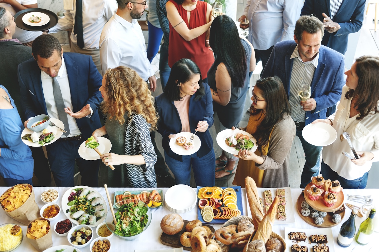 Menschen bei einem Buffet mit verschiedenen Speisen wie Salaten, Brot, Obst und Desserts bei einer Party.