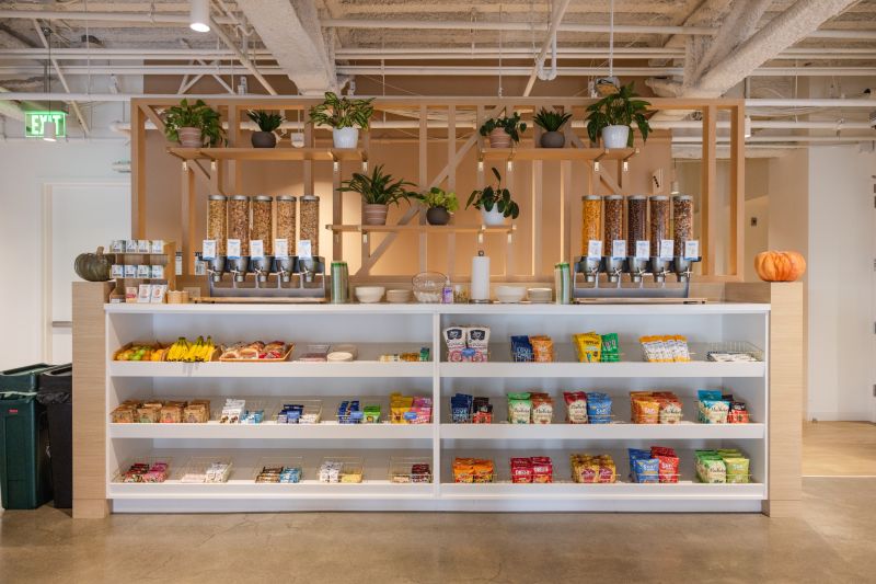 Moderne Snack-Theke mit Müsli-Spendern, Bananen, Snacks und Pflanzen in einem gut beleuchteten Raum.
