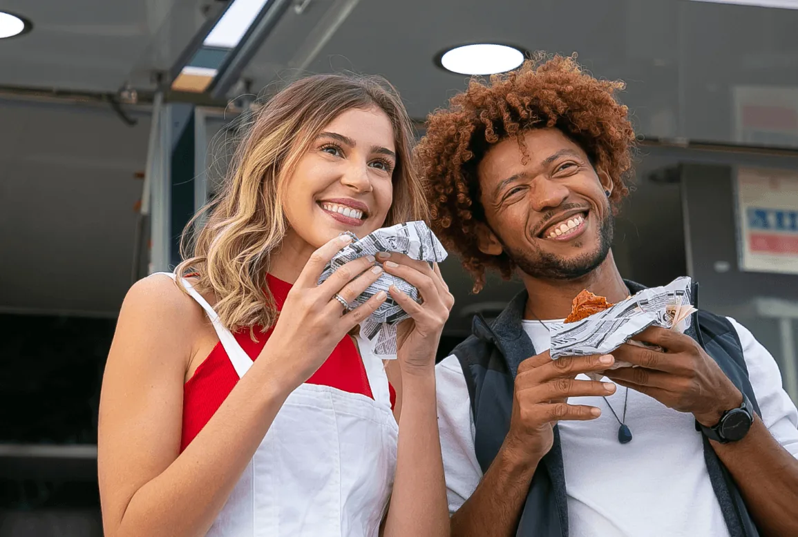 Ein lächelndes Paar isst gemeinsam Burger vor einem Foodtruck.