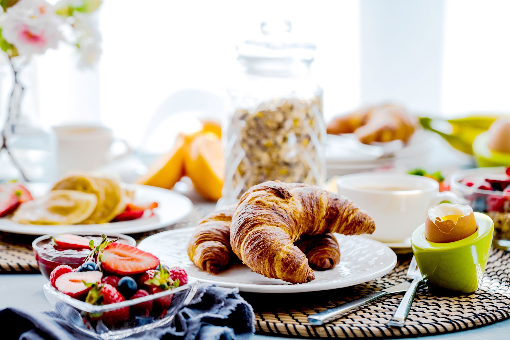 Vier lachende junge Erwachsene, zwei halten eine bunte Schüssel mit Salat und Falafel vor einem orangefarbenen Hintergrund.