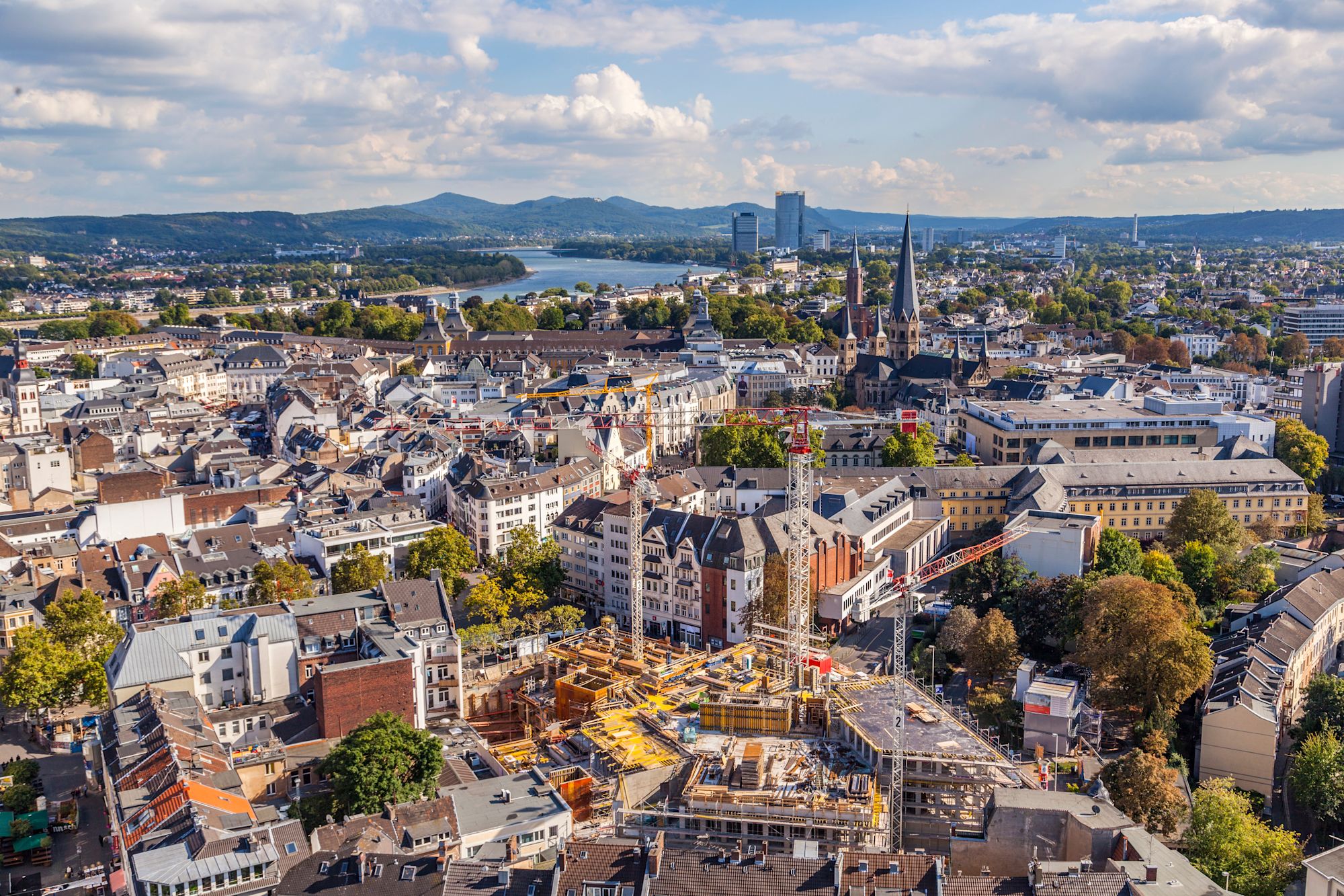 Vier lachende junge Erwachsene, zwei halten eine bunte Schüssel mit Salat und Falafel vor einem orangefarbenen Hintergrund.