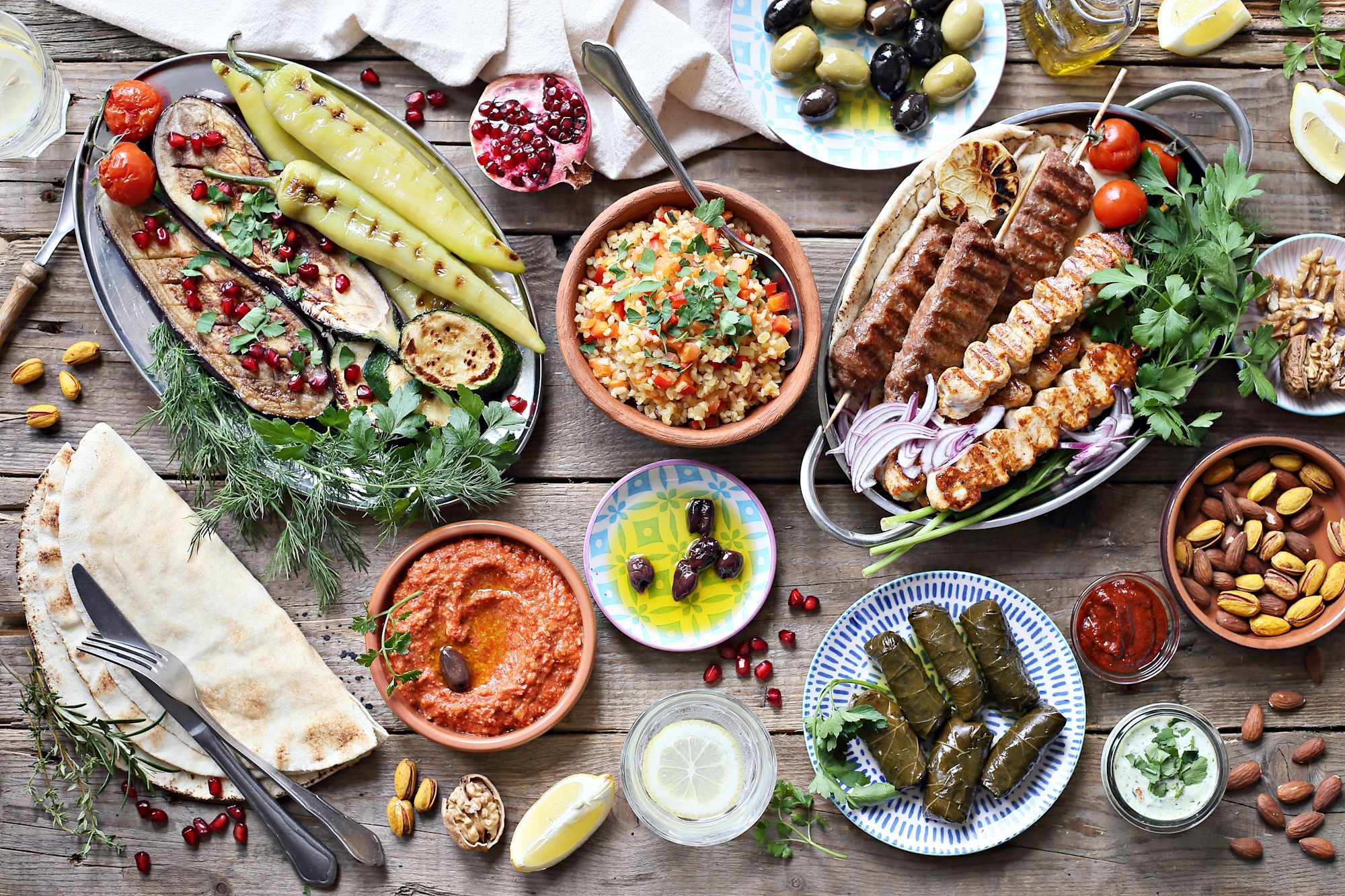 Vier lachende junge Erwachsene, zwei halten eine bunte Schüssel mit Salat und Falafel vor einem orangefarbenen Hintergrund.