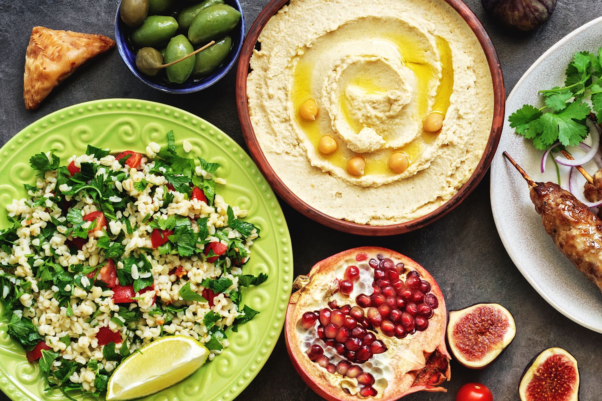 Vier lachende junge Erwachsene, zwei halten eine bunte Schüssel mit Salat und Falafel vor einem orangefarbenen Hintergrund.